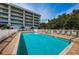 Beautiful in-ground pool with lounge chairs around the patio, with condo building in the background at 19519 Gulf Blvd # 203, Indian Shores, FL 33785