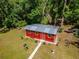 Aerial view of a red outbuilding with a gray roof, surrounded by green grass and trees at 11120 Lu Wista Ln, Brooksville, FL 34601