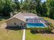 Aerial view of an enclosed pool area with a neutral colored home and green lawn at 11120 Lu Wista Ln, Brooksville, FL 34601
