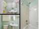 A bright bathroom featuring a pedestal sink, shower with yellow and green floral curtain and clean white fixtures at 1310 Hilton Pl, Tampa, FL 33604