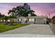 Charming single-story home with a well-manicured lawn, brick driveway, and beautiful trees under a colorful sunset sky at 2004 Yale Ave, Dunedin, FL 34698