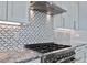 Close-up of a modern kitchen with stainless steel gas range, vent hood, marble counters, and decorative tile backsplash at 371 12Th Ave, Indian Rocks Beach, FL 33785