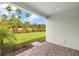 Covered back patio with brick flooring offering a view of the landscaped backyard with palm trees at 20417 Symphony Pl, Venice, FL 34293