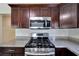 Close-up of a modern stainless steel gas range and microwave with granite countertops and wooden cabinets at 6110 N Suwanee Ave, Tampa, FL 33604