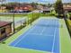 View of a blue tennis court with green trim surrounded by a fence in a residential neighborhood at 27012 Sea Breeze Way, Wesley Chapel, FL 33544