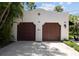 Garage with two bays and dark wood doors, decorated with ceramic tiles, surrounded by lush tropical plants at 3212 W Fountain Blvd, Tampa, FL 33609