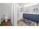 Bathroom showcasing blue cabinets, double sinks, marble shower and floors and a decorative rug at 4831 Rosatti Rd, Wesley Chapel, FL 33543