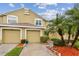 Townhouse featuring attached garage, neutral toned stucco exterior, and tidy landscaping with palm trees at 11162 Kapok Grand Cir, Madeira Beach, FL 33708