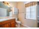 Bright bathroom features a wooden vanity, white cabinets, grab bars, and a window with blind at 445 Noble Faire Dr, Sun City Center, FL 33573