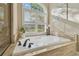 A luxurious white soaking tub with travertine surround beneath a window with white shutters at 2712 Clubhouse Dr, Plant City, FL 33566