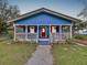 Charming blue home featuring a welcoming covered porch, red door, and freshly landscaped yard at 3213 E Genesee St, Tampa, FL 33610