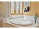 Large soaking tub with tile surround, floral curtains, and decorative accents in a bright bathroom at 10229 Waterside Oaks Dr, Tampa, FL 33647