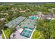 An aerial view features tennis courts, pickleball courts, a pool, and a clubhouse surrounded by lush greenery in a gated community at 10229 Waterside Oaks Dr, Tampa, FL 33647