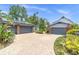 Brick paved driveway showing two garages, tropical landscaping, and mature trees against a blue sky at 13533 Bay Lake Ln, Tampa, FL 33618