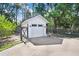 A detached garage with a white exterior, black roof, and an asphalt driveway, complemented by surrounding greenery at 3440 Crenshaw Lake Rd, Lutz, FL 33548