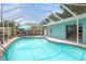 Screened-in pool area with clear blue water, lounge furniture, and a turquoise painted house at 811 Woodley Rd, Clearwater, FL 33764