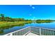 Tranquil lake with a wooden dock and metal railing, reflecting the clear blue sky, with lush greenery along the shore at 3907 Orchard Hill Cir, Palm Harbor, FL 34684