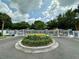 View of the community's gated entrance with white fencing and a landscaped roundabout at 1118 Kennewick Ct, Wesley Chapel, FL 33543