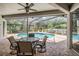 Relaxing screened-in pool area with brick pavers, ceiling fan, table with four chairs, and lush green landscaping at 5109 Hartwell Loop, Land O Lakes, FL 34638