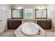 Bright bathroom with a soaking tub between two dark wood vanities, each topped with granite and illuminated by vanity lighting at 5117 Longspur Ct, Lithia, FL 33547