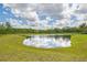 Beautiful tranquil pond surrounded by green grass and trees, reflecting blue skies and fluffy white clouds at 16712 Courtyard Loop, Land O Lakes, FL 34638