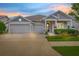 Charming one-story home at dusk featuring a three-car garage and beautifully landscaped front yard with colorful flowers at 4166 Epic Cv, Land O Lakes, FL 34638