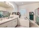 Bright bathroom with double sinks, a tub, tiled flooring, and a large window, offering a spa-like retreat at 14985 Alan Ct, Largo, FL 33771