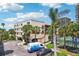 Condominium building with a tiled roof, palm trees, and a view of a tennis court and a van parked in front at 7564 Bayshore Dr # 302, Treasure Island, FL 33706