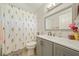 Well-lit bathroom featuring a floral shower curtain, grey vanity, and modern fixtures at 1447 Stetson Dr, Wesley Chapel, FL 33543