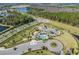 Aerial view of a community pool and playground featuring a roundabout, lake, and lush landscaping at 32242 Summerglade Dr, Wesley Chapel, FL 33545