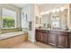 Bright bathroom featuring a soaking tub with decorative tile, and a granite-topped double vanity at 9317 Bella Vita Cir, Land O Lakes, FL 34637