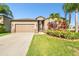 A one-story home features a two-car garage, neutral siding and manicured landscaping with tropical accents at 13201 Wellington Hills Dr, Riverview, FL 33579