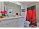 Bathroom with double sinks, a large mirror, vanity cabinets, decorative flowers and black and red shower curtain at 2858 Star Anise Ln, Wimauma, FL 33598