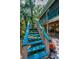 Colorful blue stairs leading to a charming home with a screened porch, surrounded by lush landscaping and mature trees at 420 Hanby St, Crystal Beach, FL 34681