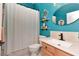 Bright bathroom featuring turquoise walls, oval mirror, wood shelves, and a white vanity with a light wood cabinet at 5103 Rushbrook Rd, Land O Lakes, FL 34638
