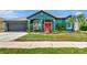 Charming home exterior with teal paint, a red front door, landscaping, and a two-car garage at 5103 Rushbrook Rd, Land O Lakes, FL 34638
