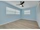 Light blue bedroom features wood floors, ceiling fan, and two windows at 1624 Chateau Dr, Clearwater, FL 33756