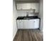 Kitchenette area featuring ample white cabinets, stainless steel sink, black countertop, and hardwood flooring at 7525 Arbordale Dr, Port Richey, FL 34668