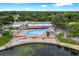 Aerial view of a community pool area with ample seating, a clubhouse, and a picturesque lake at 10820 Hachita Dr, Port Richey, FL 34668