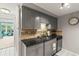 Compact kitchen featuring gray cabinetry, tile backsplash, dark granite countertop, and stainless steel dishwasher at 4305 Summersun Dr, New Port Richey, FL 34652