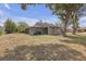 Backyard view of a gray house featuring mature trees, an open lawn, and easy access to the carport at 4623 Wisteria Dr, Zephyrhills, FL 33542
