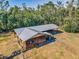Aerial shot showcases a weathered barn with a metal roof and an adjacent shelter within a grassy, tree-lined area at 8755 Ogleby Creek Rd, Myakka City, FL 34251
