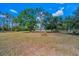 Expansive green lawn with scattered trees leading to a charming home with a light-colored exterior and a welcoming yard at 8755 Ogleby Creek Rd, Myakka City, FL 34251