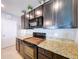 Close-up of a well-equipped kitchen with granite countertops, a dark cooktop, and sleek, dark cabinetry at 11013 Leland Groves Dr, Riverview, FL 33579