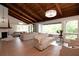 Bright living room features wood-beam ceiling, white brick fireplace, and large windows overlooking the landscaped yard at 1296 Weybridge Ln, Dunedin, FL 34698
