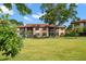 Multi-story tan apartment building features balconies and a lawn with mature trees on a sunny day at 12900 Vonn Rd # F101, Largo, FL 33774