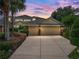 Two-car garage with stone accents, mature landscaping, and a wide driveway under a stunning dusk sky at 13209 Palmilla Cir, Dade City, FL 33525