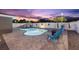 Twilight view of the swimming pool with chairs and firepit on the grey paver patio and a beautiful sky at 895 Joan St, Dunedin, FL 34698