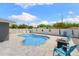 A beautiful pool, chairs, and firepit sit on a grey paver patio with a white fence and blue sky in the background at 895 Joan St, Dunedin, FL 34698