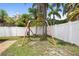 Large backyard featuring a swing set surrounded by lush palm trees and a white fence at 11619 Fox Creek Dr, Tampa, FL 33635